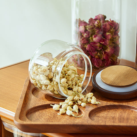 Small jar from the Acacia glass storage jar set spilling dried flowers on a wooden tray
