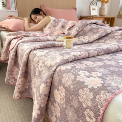 Woman wrapped in blush floral summer blanket relaxing in bed with soft lighting and warm decor