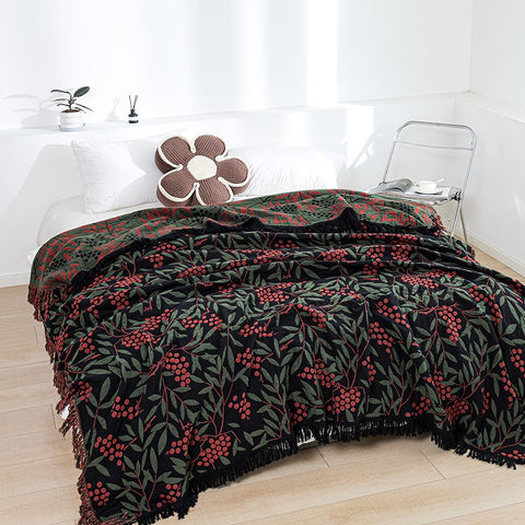 Black cotton throw blanket with red berries and green leaf design on bed