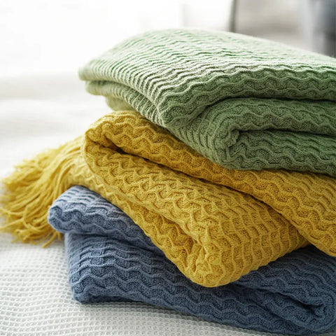 Stack of folded textured blankets in green, yellow, and blue on a light surface.