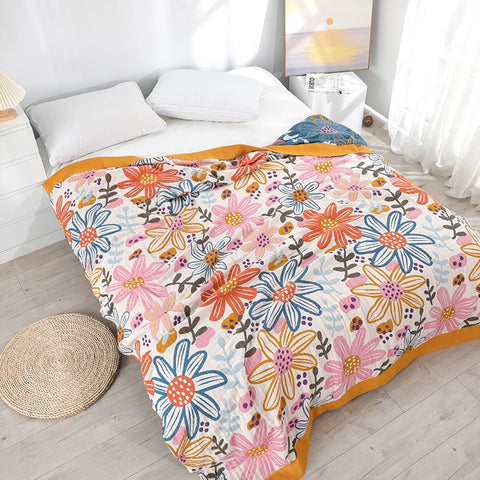 Floral cotton summer blanket with orange border laid on white bed