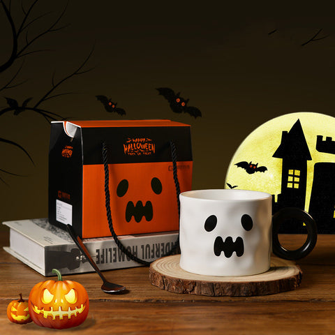 Halloween-themed mug with ghost design, pumpkin, and gift box on a wooden surface.