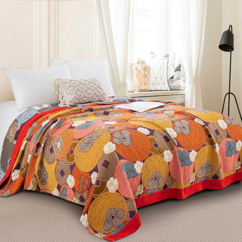 Persimmon Bloom cotton blanket with vibrant floral pattern spread over queen bed in cozy bedroom setting