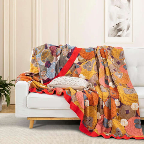 Persimmon Bloom cotton blanket draped on white sofa showing floral and fruit pattern with vibrant red border