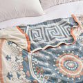 Close-up of soft cotton throw blanket with intricate blue and orange geometric patterns on a bed with white bedding.