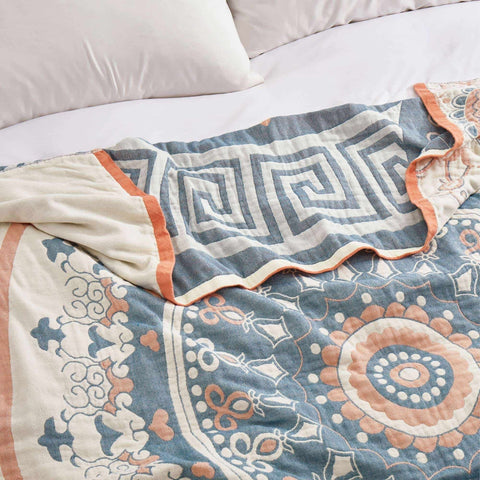 Close-up of soft cotton throw blanket with intricate blue and orange geometric patterns on a bed with white bedding.