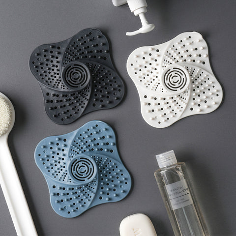 Three silicone bath mats in black, white, and blue on a gray surface with bathroom products.