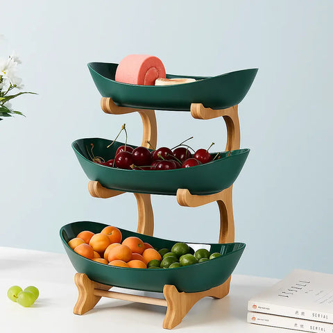 3-tier green ceramic bamboo fruit basket filled with oranges, cherries, and grapes on kitchen counter