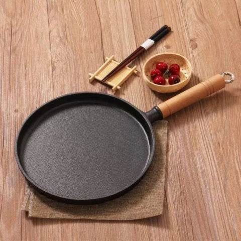 Cast iron frying pan next to chopsticks and cherries on wooden table