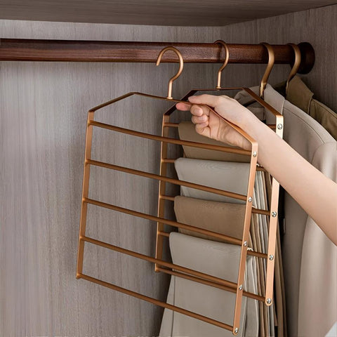 Hand using a gold multi-tiered hanger to organize clothes in a closet.