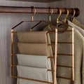 Gold hanger organizer with clothes on a wooden rod against a neutral wall.