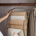 Hand holding a gold hanger with folded clothes against a neutral background
