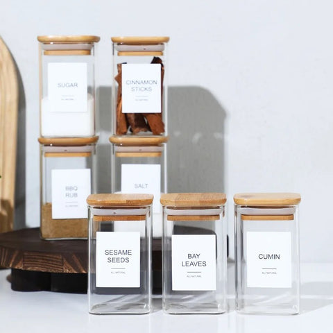 Bamboo spice jars stacked on wooden board with labels for sugar, salt, cinnamon.
