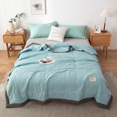 Bed with light blue summer quilt and pillows in a bedroom setting.