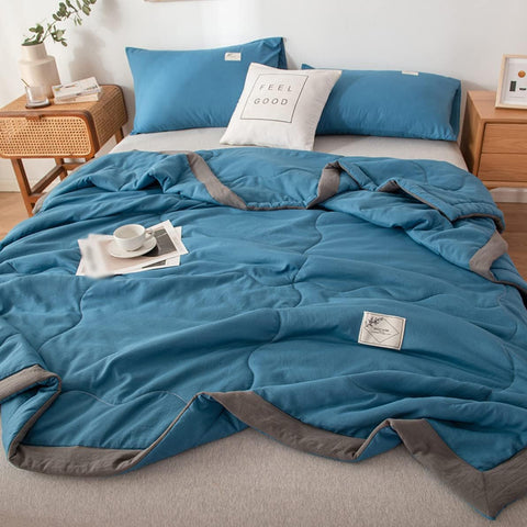 Blue quilt with gray trim on a bed in a bedroom setting.