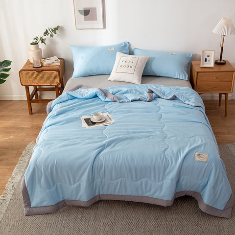 Blue summer quilt set on a bed in a bedroom with side tables and decor.