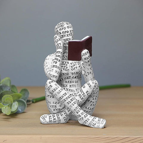 Decorative figure made of printed paper sitting and reading a book on a wooden surface.