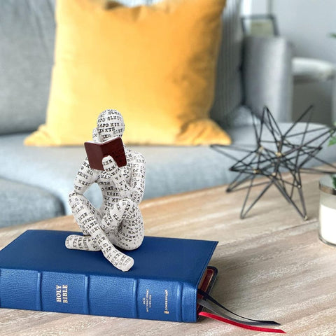 Decorative sculpture of a person wrapped in text sitting on a blue book with a blurred indoor background.
