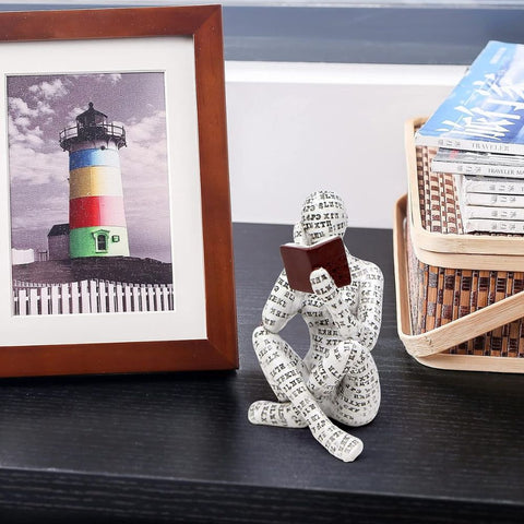Decorative statue of a person made from paperclips on a shelf with a framed picture of a lighthouse and a basket of books.