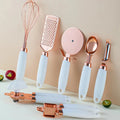 Set of kitchen utensils with rose gold and white handles on a beige background