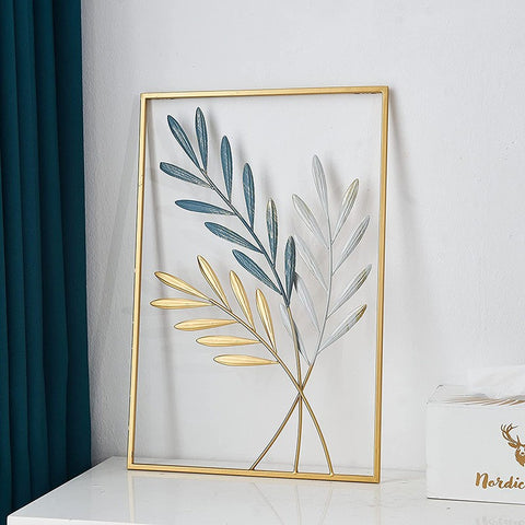 Decorative wall art with leaf design in a gold frame on a white surface.