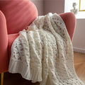 White knitted blanket on a pink armchair with a cup.
