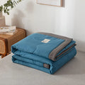 Folded blue and gray quilt on a bed in a bedroom setting.