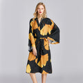 Woman wearing a black and orange floral ginko bathrobe pajama on a gray background