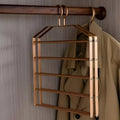 Gold hanger with multiple hooks attached to a wooden rod against a neutral wall.