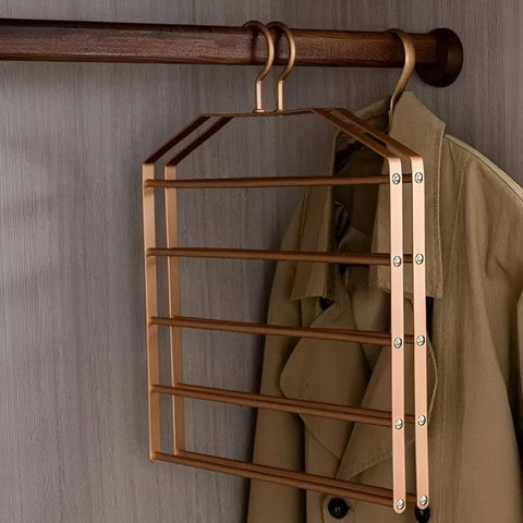 Gold hanger with multiple hooks attached to a wooden rod against a neutral wall.