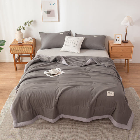 Gray quilt set on a bed in a bedroom with wooden nightstands and decor.