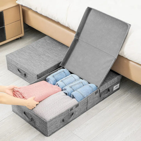 Gray storage container with clothes being placed inside on a wooden floor.