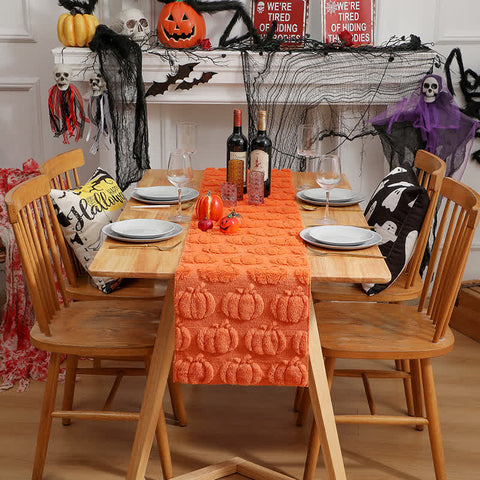 Dining table set for Halloween with an orange pumpkin-patterned table runner, wine bottles, and decorative items.