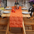 Dining table set with an orange pumpkin-patterned table runner, wine bottles, and Halloween-themed decor.