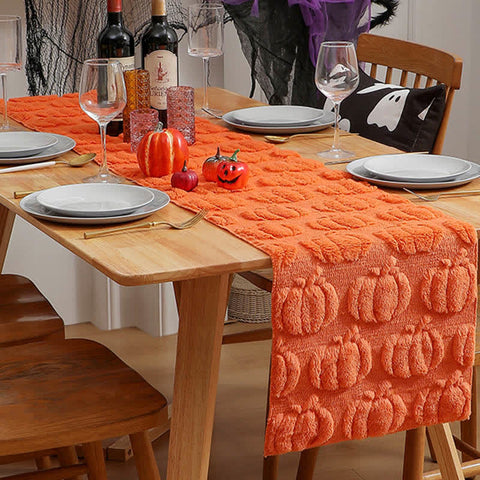 Dining table set for Halloween with an orange pumpkin-patterned runner, wine bottles, and decorative pumpkins.