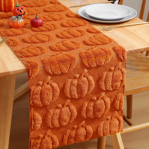 Orange pumpkin-patterned table runner on a wooden table with decorative pumpkins.