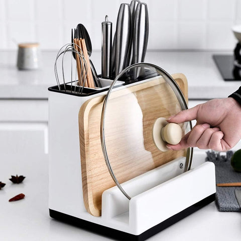 Kitchen utensil holder with cutting board and ladle, hand placing a lid on a white surface.