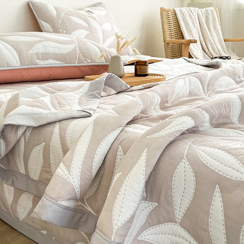 Bed with leaf patterned bedding and pillows in a cozy room setting.