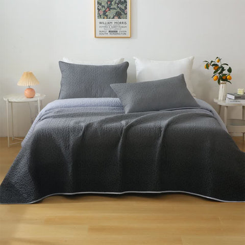 Gray quilt and pillows on a bed in a bedroom setting with decor elements.