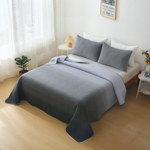 Gray blanket draped over a bed in a bedroom with light wood flooring and white walls.