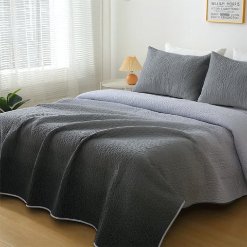 Gray quilted coverlet on a bed with pillows in a bedroom setting.
