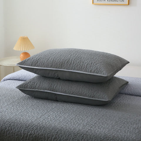 Two gray textured pillows on a bed with a lamp and wall art in the background.