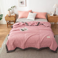 Pink quilt on a bed in a bedroom setting with side tables and decor.