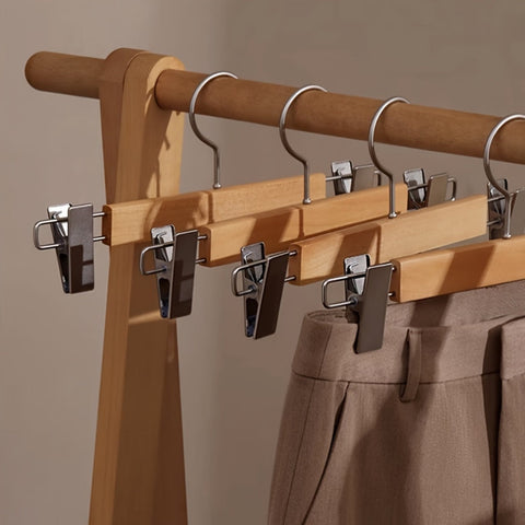 Wooden hanger with clips holding a pair of pants against a neutral background