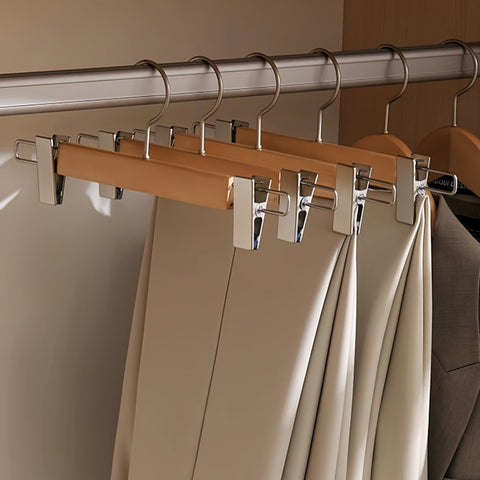 Wooden hangers with metal clips holding clothes on a rod against a neutral background