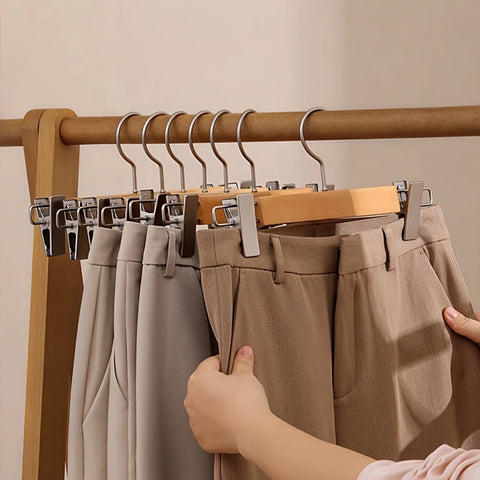 Person selecting a pair of beige pants from a rack with multiple pairs hanging on hangers.