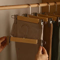 Person using a multi-clip hanger to hang multiple pairs of pants on a wooden rod.