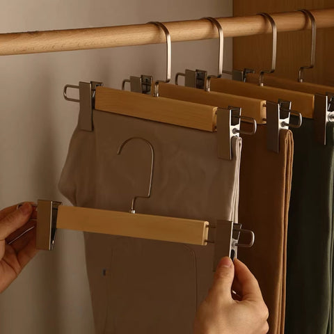 Person using a multi-clip hanger to hang multiple pairs of pants on a wooden rod.