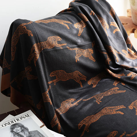 Black blanket with brown animal patterns draped over a surface, with a magazine underneath.