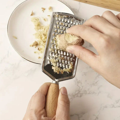 Person using a metal grater to shred ginger on a marble surface